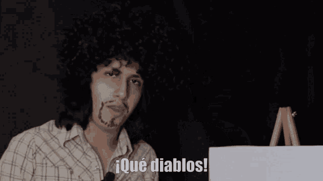 a man wearing a wig and a plaid shirt says " ique diablos "