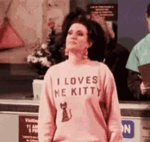a woman wearing a pink sweater that says `` i loves me kitty '' is standing in a store .