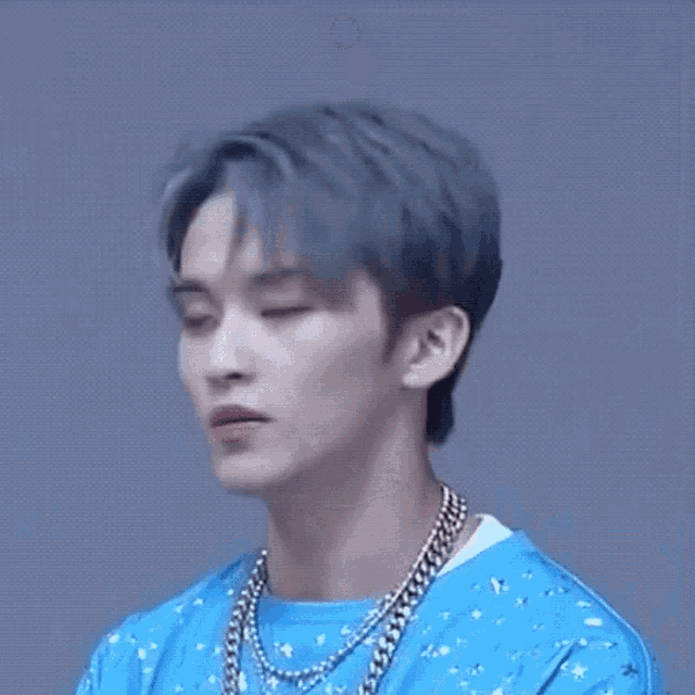 a close up of a young man with blue hair wearing a blue shirt and a necklace .