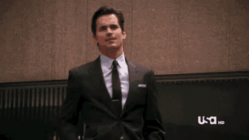 a man in a suit and tie is standing in front of a building and looking at the camera .