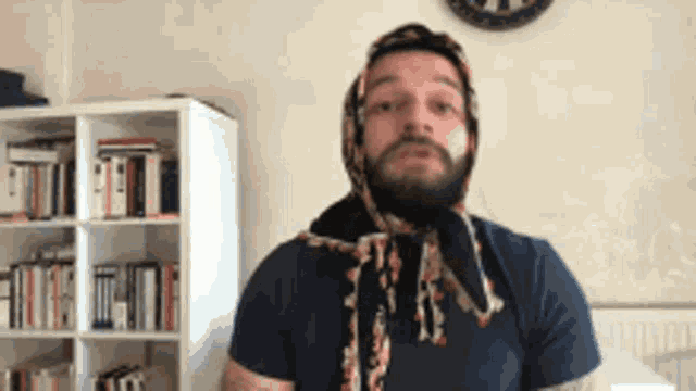 a man with a scarf around his head is standing in front of a book shelf