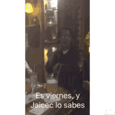 a man is sitting at a table with a drink and the words es viernes y jaicec lo sabes