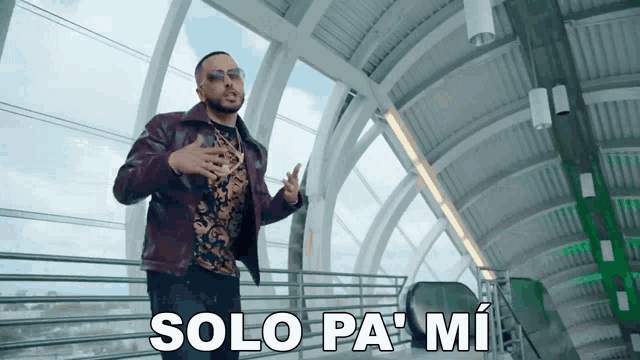 a man wearing sunglasses and a leather jacket stands in front of an escalator and says solo pa mi