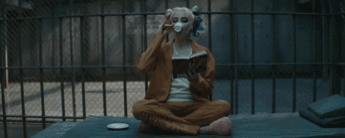 a woman in a suicide squad costume is sitting on a bed reading a book and drinking tea .
