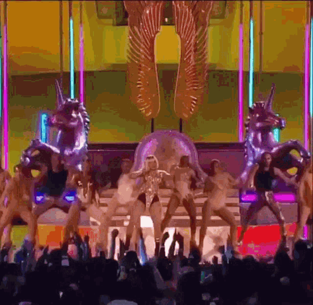 a group of women are dancing on a stage with unicorns and wings