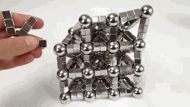 a person is holding a piece of metal that looks like a cube and balls