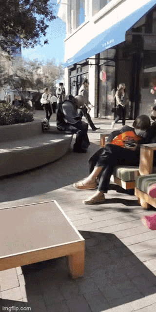 a man sits on a bench in front of a store with a blue awning that says ' the west '