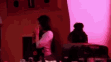 a blurry picture of a woman sitting in front of a pink wall holding a drink .