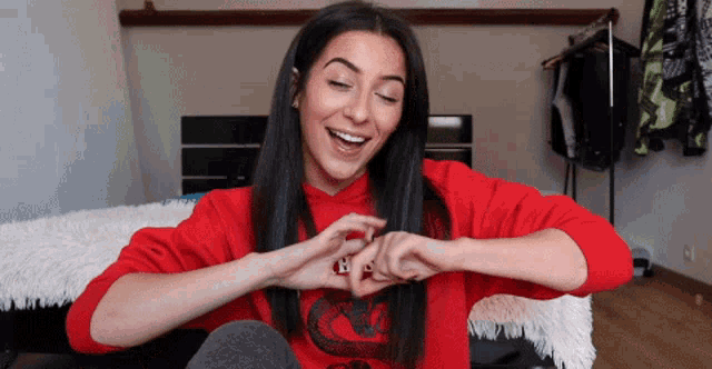 a woman wearing a red sweatshirt with a snake on it is making a heart shape with her hands