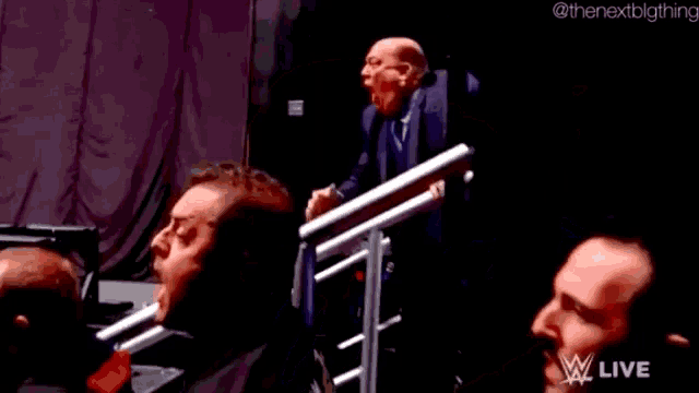 a bald man is yawning while watching a wrestling match on a television .