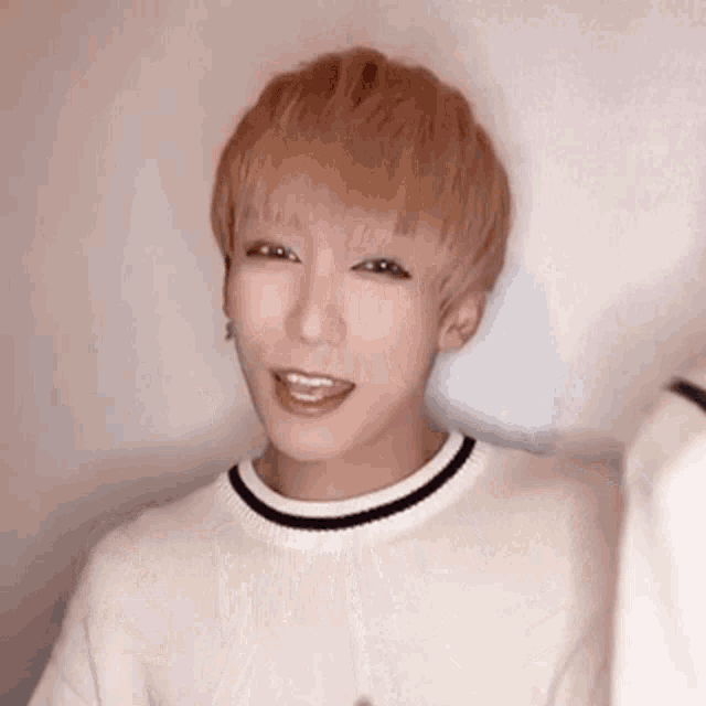 a young man with blonde hair is wearing a white sweater with a black stripe around the neck .