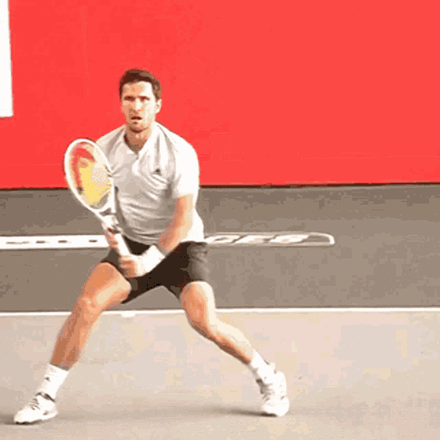 a man is holding a tennis racquet in front of a red wall that says ore on it