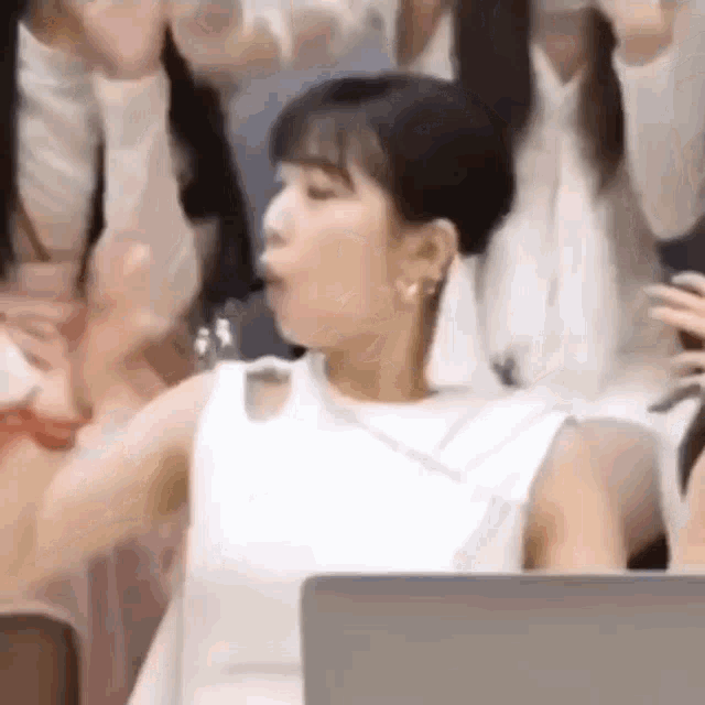 a woman in a white dress is sitting in front of a laptop computer and making a funny face .