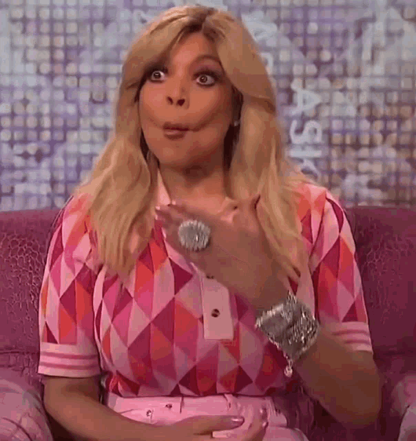 a woman is sitting on a couch making a funny face while wearing a pink shirt .