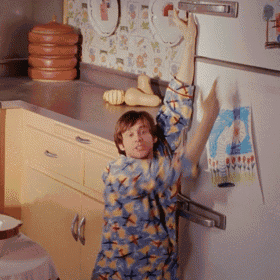 a man in a blue and yellow shirt is reaching up to open a refrigerator