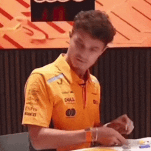 a man in a yellow shirt is sitting at a table eating a piece of pizza .
