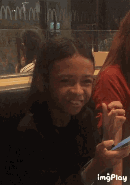 a girl is smiling while looking at a cell phone with imgplay written below her