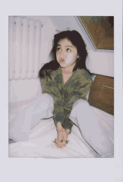 a woman in a green plaid shirt is sitting on a bed