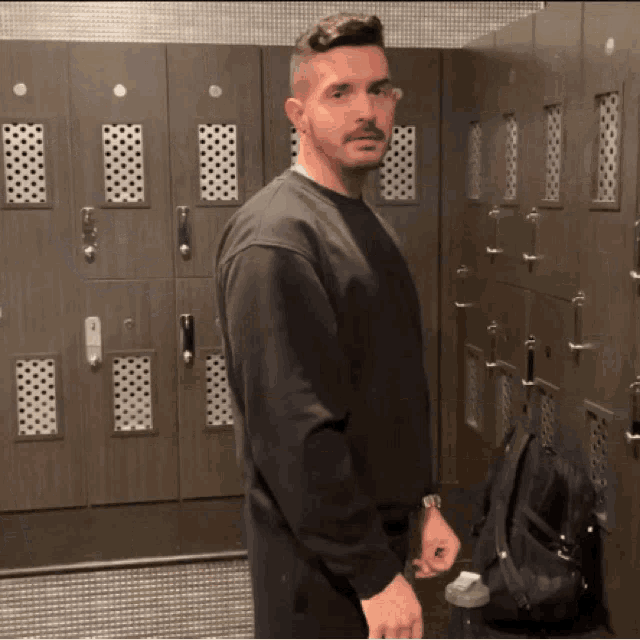 a man standing in a locker room with a backpack