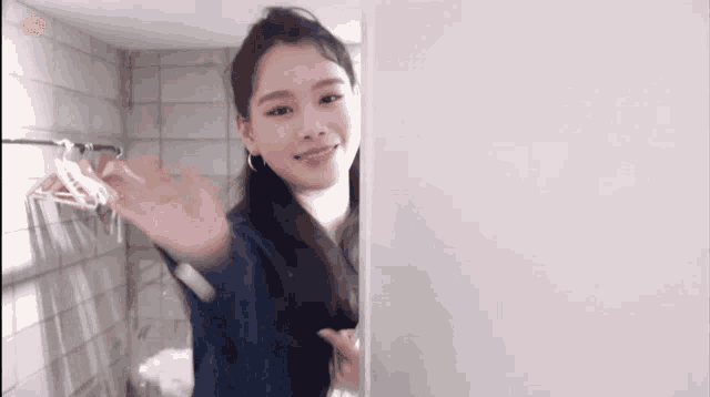 a woman is waving from behind a wall in a room with clothes hanging on the wall .