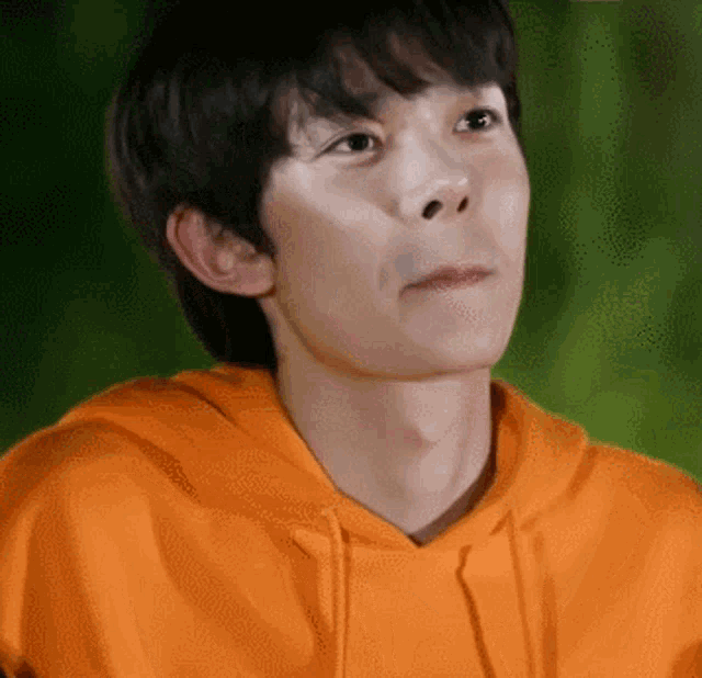 a young man wearing an orange hoodie is making a face .
