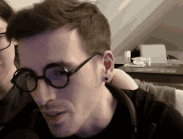 a man wearing glasses and a black shirt looks at something