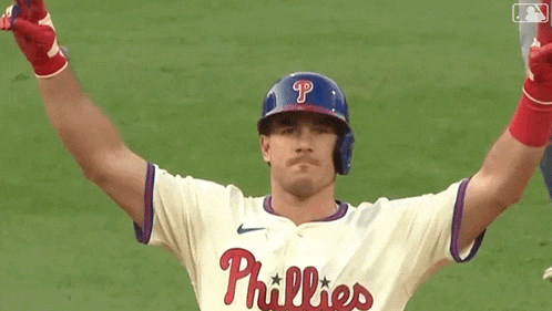 a baseball player wearing a phillies jersey and helmet is standing on a field with his arms in the air .
