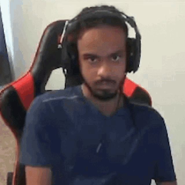 a man with a beard is wearing headphones while sitting in a red and black chair .