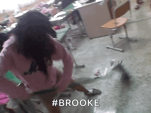 a girl in a pink sweater is standing in a classroom with the word brooke written on the floor
