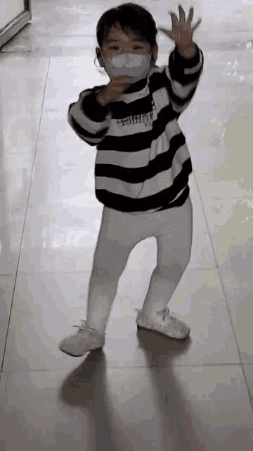 a little boy wearing a mask and striped shirt is dancing on a tiled floor .