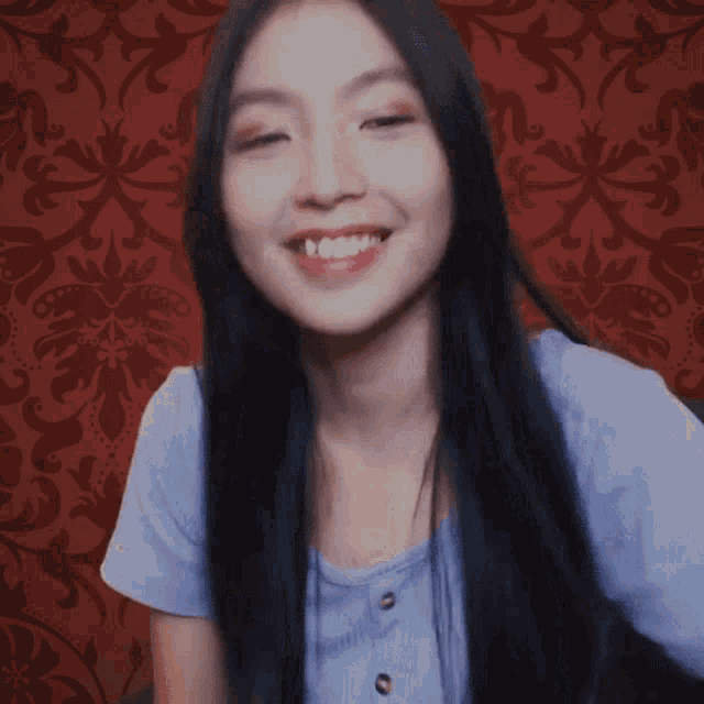 a woman with long black hair is smiling in front of a red background