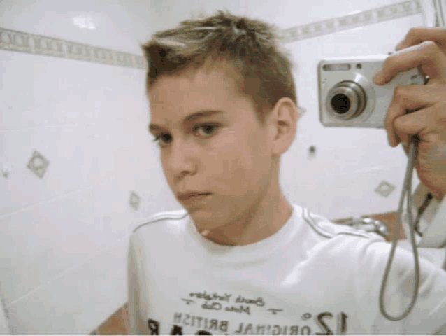 a young boy is taking a picture of himself with a camera in a bathroom