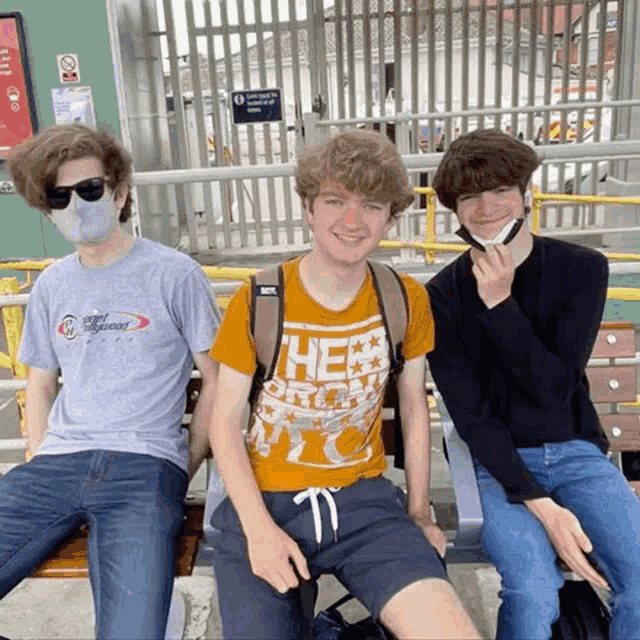 three young men wearing face masks are sitting on a bench with one wearing a shirt that says " the north face "