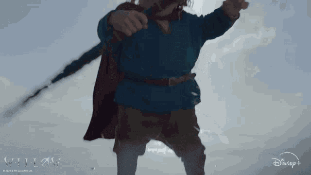 a man in a blue shirt and red cape is holding a sword in front of a disney + logo