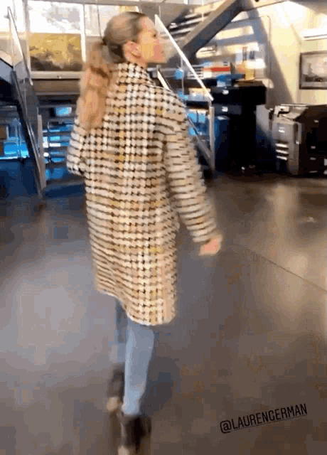 a woman in a plaid coat is dancing in front of stairs and a sign that says laurengerman