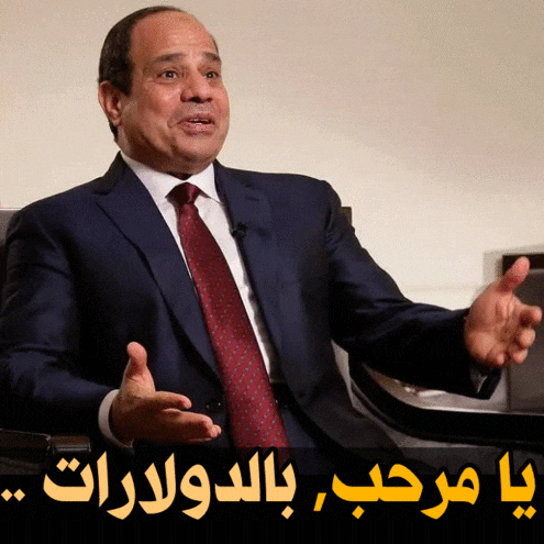 a man in a suit and tie is sitting in front of a sign in arabic