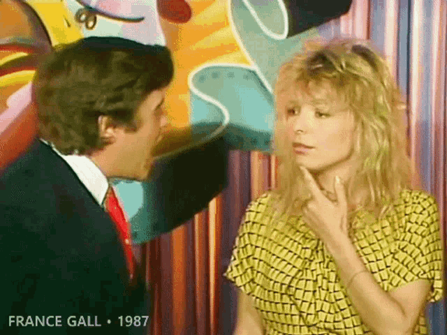 a man in a suit and tie is talking to a woman in a yellow shirt and the year 1987 is on the bottom