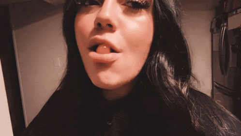 a close up of a woman 's face with a black fridge in the background