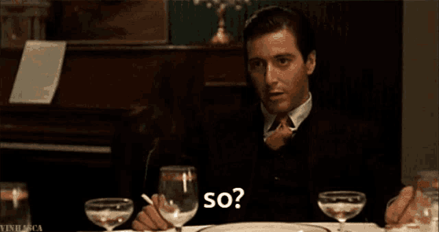 a man sitting at a table with a glass of wine and a cigarette in his hand says so