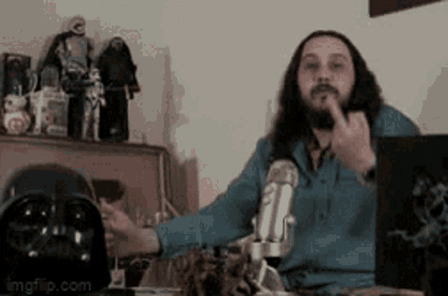 a man with long hair and a beard is sitting in front of a microphone giving the middle finger .