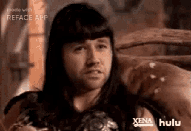 a man with long hair and a beard is sitting on a couch with his arms crossed .
