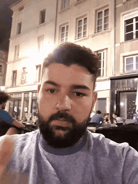 a man with a beard is taking a selfie in front of a building that says " bistro " on it
