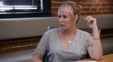 a woman is sitting at a desk in front of a brick wall and talking to someone .
