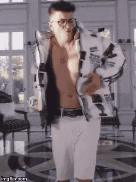 a shirtless man wearing glasses and a white jacket is standing in a living room .