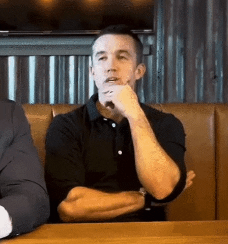 a man in a black shirt is sitting at a table with his arms crossed .