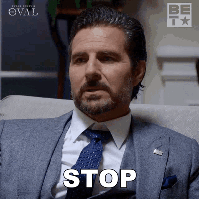a man in a suit and tie is sitting in a chair and says stop