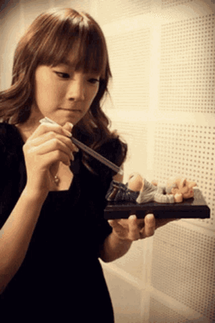 a woman in a black dress is holding a small figurine of a man laying down
