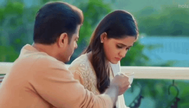 a man and a woman are sitting next to each other on a balcony drinking tea .