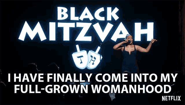 a woman singing into a microphone in front of a sign that says black mitzvah