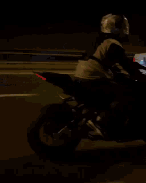 a person riding a motorcycle on a highway at night with a green sign in the background